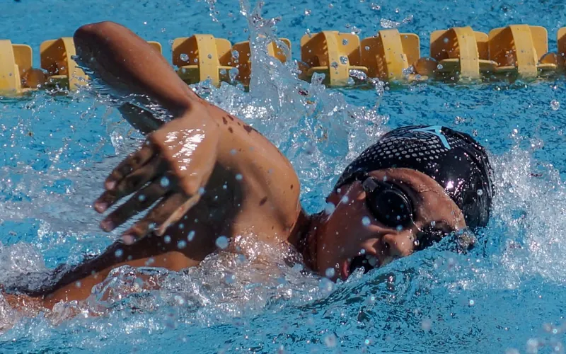 Nadador de estilo libre con gorra negra levantando el brazo fuera del agua durante un entrenamiento de natación